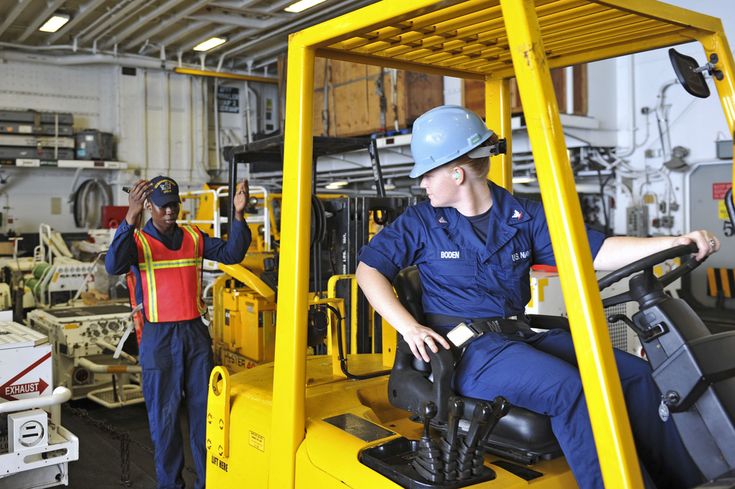 Operador de montacargas con casco azul y guía de seguridad dirigiendo maniobra en almacén industrial